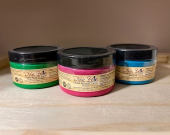 May include: Three 4 oz jars of Dixie Belle Chalk Mineral Paint. The jars are labeled Tree Frog Green, Peony, and Peacock. The paint is a popular choice for furniture and home decor projects.