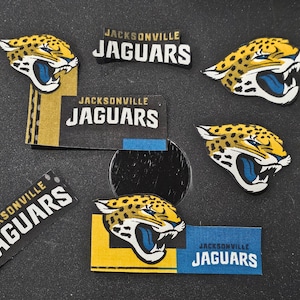 May include: Five Jacksonville Jaguars stickers with the team logo and name. The stickers are on a black surface.