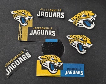 May include: Five Jacksonville Jaguars stickers with the team logo and name. The stickers are on a black surface.