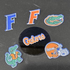 May include: Assorted patches and a circular emblem featuring the Florida Gators logo. Includes the letter "F" in blue and orange, a Gator mascot, and a football helmet. The word "Gators" is also displayed.