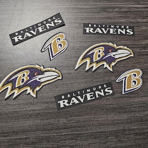 May include: Five iron-on patches featuring the Baltimore Ravens logo. The patches are black, purple, and gold with the team name and logo.