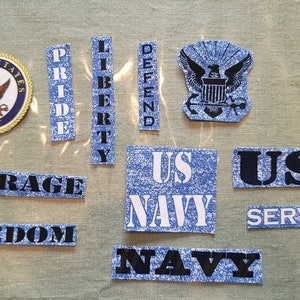 May include: A collection of blue and white fabric patches with text and images. The patches include the words "United States Navy", "Pride", "Liberty", "Defend", "Courage", "Freedom", "US Navy", "USA Service", and "Navy". There is also a patch with an eagle and the words "United States Navy".