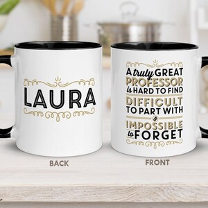 Pu&ograve; includere: Tazza in ceramica bianca con manico e bordo neri. Un lato presenta il nome "LAURA" in nero e oro. L'altro lato recita "A truly GREAT PROFESSOR is HARD TO FIND DIFFICULT TO PART WITH & IMPOSSIBLE to FORGET."