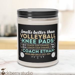 May include: A white candle jar with a black lid and a black and white label. The label says "Smells better than Volleyball Knee Pads" and "A Good Coach Can Change A Meet, A Great Coach Can Change A Life!"  The label also says "Coach Ethan" and "Woodland Eagles 2023-2024".
