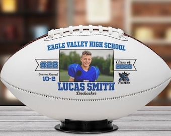 Puede incluir: Balón de fútbol blanco con un diseño azul y blanco. El balón de fútbol tiene una foto de un joven con un uniforme de fútbol, el texto "Eagle Valley High School", "#22", "Season Record 10-2", "Lucas Smith", "Linebacker", "Class of 2020" y un logotipo de equipo.