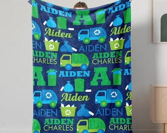 May include: A blue fleece blanket with a repeating pattern of green and blue garbage trucks, green recycling bins, and the name "Aiden" in a blue and green font.