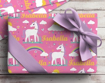 Könnte beinhalten: Rosa Geschenkpapier mit einem Einhorn- und Regenbogenmuster. Das Papier ist mit dem Namen "Isabella" verziert, der sich wiederholt. Ein lila Band ist um das Geschenk gebunden.