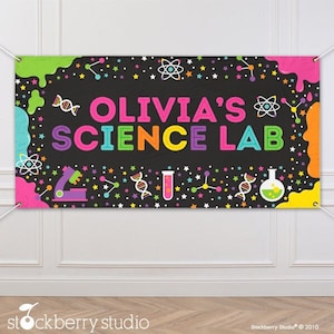 May include: A black banner with the text "Olivia's Science Lab" in colorful letters. The banner is decorated with stars, atoms, beakers, test tubes, and DNA strands.