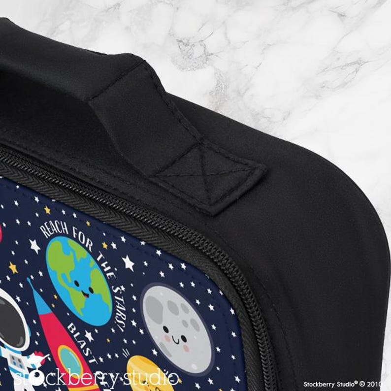 Puede incluir: Bolsa de almuerzo negra con un dise&ntilde;o espacial. La bolsa presenta un fondo azul marino con ilustraciones de planetas, estrellas, un cohete y un astronauta. El texto en la bolsa dice "Reach for the Stars" y "Blast Off". Se ven un asa y una cremallera negras.