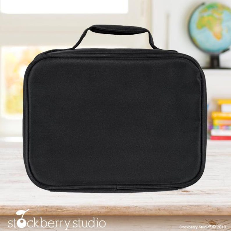 Puede incluir: Una bolsa de almuerzo negra con un asa superior. La bolsa es rectangular con esquinas redondeadas y cierre de cremallera. La bolsa est&aacute; sobre una superficie de madera clara.