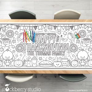 Op de afbeelding: Een witte tafelloper met een zwart omtrekontwerp, met als thema Thanksgiving, met de tekst "HAPPY THANKSGIVING! THE THOMAS FAMILY". De loper bevat illustraties van kalkoenen, pompoenen en desserts, met een set kleurpotloden.