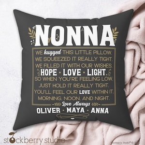 May include: A dark gray decorative pillow with the word "NONNA" in large white letters at the top. The pillow has a gold border and contains a heartfelt message. The names Oliver, Maya, and Anna are at the bottom.