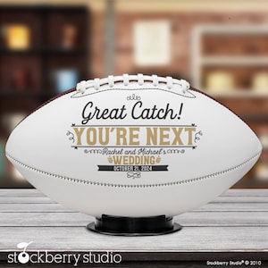 Pode incluir: Bola de futebol branca com costuras pretas e um gr&aacute;fico preto e dourado que diz "Great Catch! You're Next" com o texto "Rachel and Michael's Wedding October 21, 2024" abaixo.