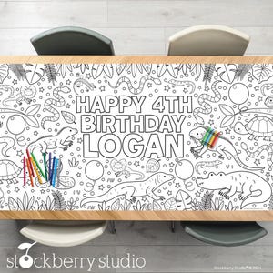May include: A black and white table runner with the text "HAPPY 4TH BIRTHDAY LOGAN" and illustrations of reptiles, balloons, and leaves. Colouring pencils are on the left side of the runner.