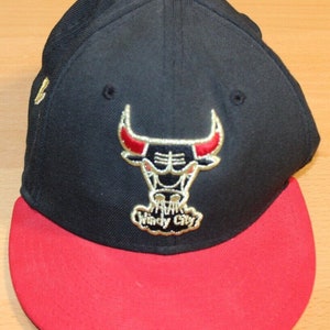 Puede incluir: Gorra de béisbol negra y roja con un logotipo bordado en oro de los Chicago Bulls que presenta una cabeza de toro y el texto "Windy City".