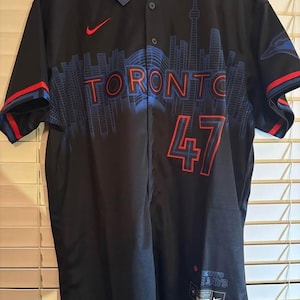 May include: Black baseball jersey featuring the word "TORONTO" in blue and red, and the number "47". The jersey has a blue skyline design, red accents, and a Nike logo. The tag reads "DIVERSITY-OUR-STRENGTH".