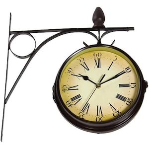 May include: Double-sided outdoor clock with a dark brown metal frame and bracket. The clock face has a cream-colored background with black Roman numerals and hands. The clock is designed to be mounted on a wall or post.