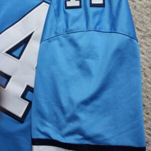 May include: A light blue football jersey with the number "14" on the sleeve and the word "CAROLINA" on the cuff.