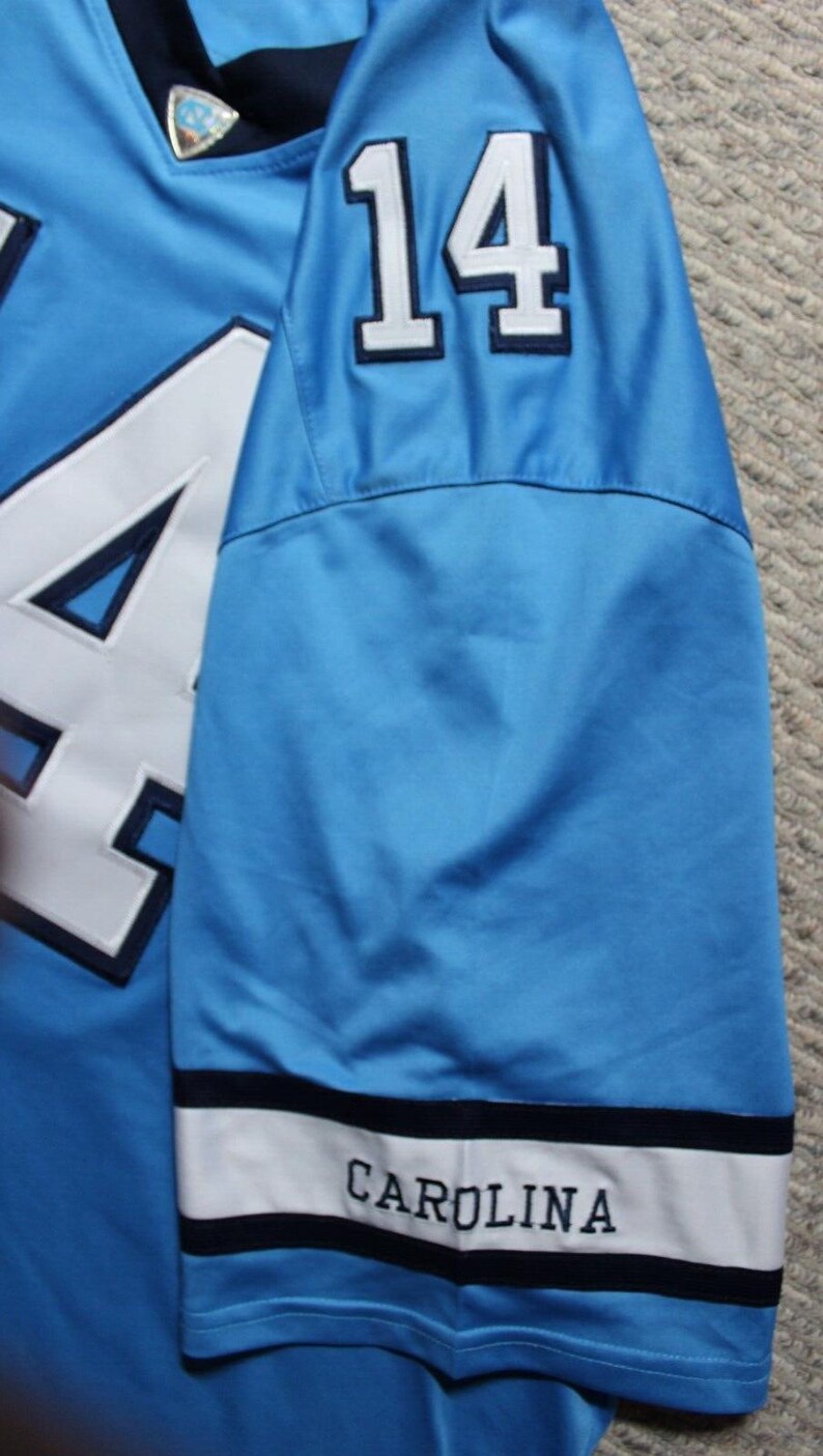 May include: A light blue football jersey with the number "14" on the sleeve and the word "CAROLINA" on the cuff.