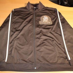 May include: Brown track jacket with white stripes down the sleeves. Features a full zipper and a patch with the word "Grumpy" and a cartoon character. The jacket has two front pockets and a stand-up collar.