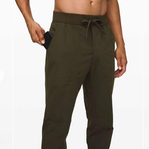 Op de afbeelding: Donker olijfgroene sportbroek met een tailleband met trekkoord en zakken. De broek heeft een relaxte pasvorm en is gemaakt van een zacht, duurzaam materiaal. Een zwarte smartphone is zichtbaar in de voorzak. Geschikt voor diverse activiteiten.