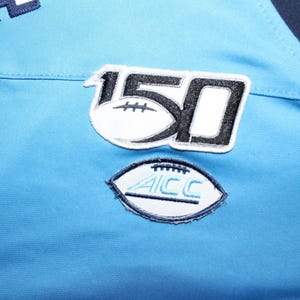 May include: A light blue jersey with a black and white patch that says "150" and a white patch with a football and the text "ACC".