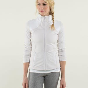 May include: A white and light grey athletic jacket with a full-length zipper. The jacket has a high collar and white shoulder panels. The fabric has a subtle grid pattern. The model is wearing grey athletic pants and a white top underneath.