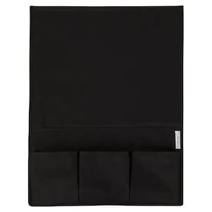 May include: A rectangular black fabric organizer featuring a large flat upper section and three smaller square pockets along the bottom edge. A small white rectangular tag with black text is attached to the side of the middle pocket.