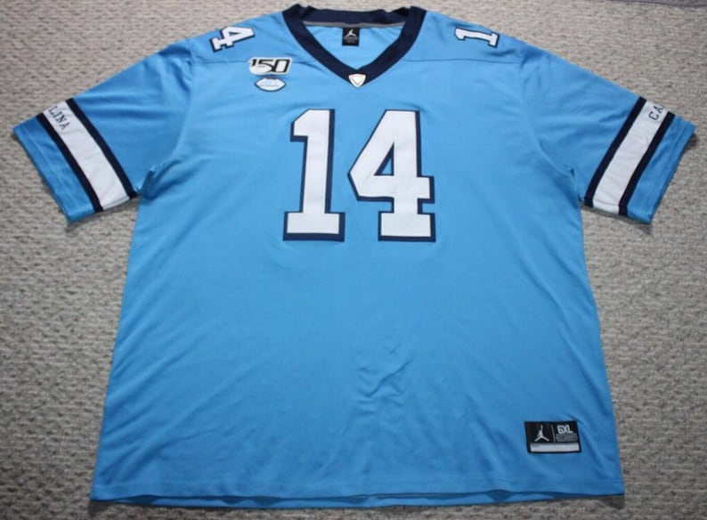 May include: A light blue football jersey with white and navy blue trim. The number "14" is printed in white on the front of the jersey. The jersey has a navy blue collar and a white stripe on each sleeve. The jersey is a size XL.