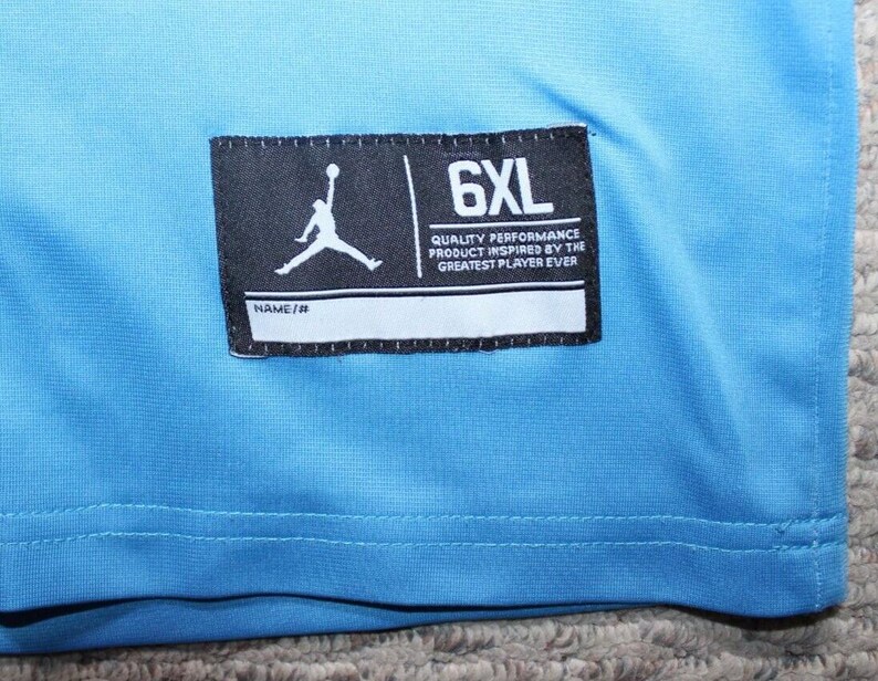 May include: A light blue t-shirt with a black tag that says "6XL" and "Quality Performance Product Inspired by the Greatest Player Ever".