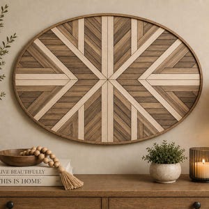 Op de afbeelding: Een ovaal wandkunstobject met een geometrisch patroon van licht- en donkerbruine houten latten, gerangschikt in een symmetrisch, stralend ontwerp. De wanddecoratie is omlijst met een dunne, bijpassende bruine houten rand voor een strak uiterlijk.