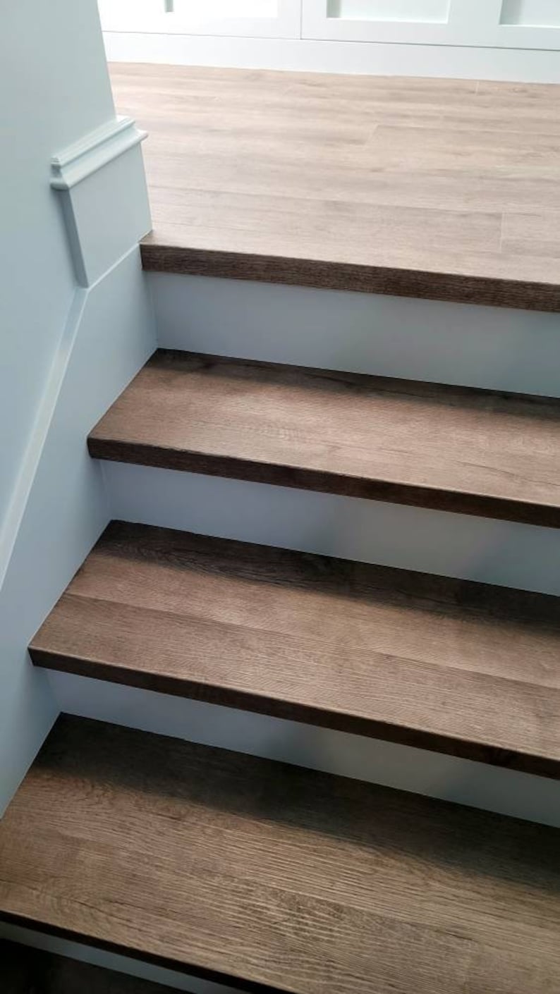 May include: A staircase featuring wooden steps and white risers. The steps are a dark brown hue, and the risers are painted white. The wall is a light blue colour. The stairs lead to a light-coloured wooden floor.