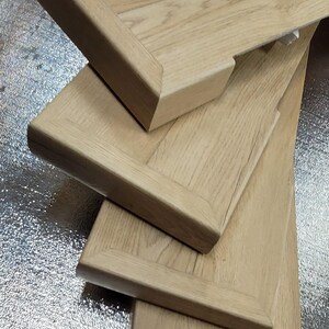 May include: Close-up of several custom luxury vinyl flooring stair tread covers with a light oak grain. The tread covers have a rectangular shape with an exposed finished end. The wood has a natural, light brown color.