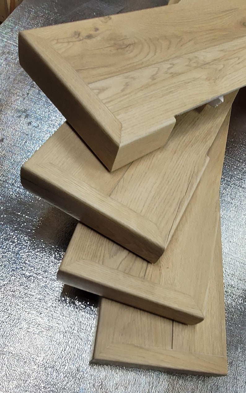 May include: Close-up of several custom luxury vinyl flooring stair tread covers with a light oak grain. The tread covers have a rectangular shape with an exposed finished end. The wood has a natural, light brown color.