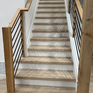 May include: A wooden staircase with light-colored treads and risers. The staircase features a wooden handrail and black metal balusters. The design is modern and minimalist, with a focus on natural materials and clean lines.