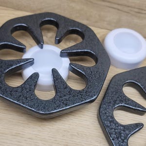May include: Two black metal stovetop burner covers with a textured finish. The covers are shaped like a flower with six petals. A white ceramic burner cover is in the center of the larger cover.