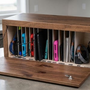 May include: A wooden charging station with multiple compartments, holding various electronic devices and charging cables. The open front reveals a series of vertical dividers, with a hinged door and a chain for support. The wood has a warm, brown finish.