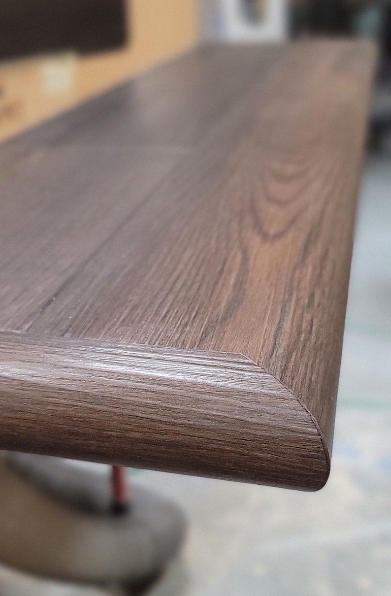 May include: Close-up of a dark brown wooden looking stair step with a beveled edge. The wood grain is visible, and the step appears to be well-crafted. The corner of the step is rounded with multiple finished sides.