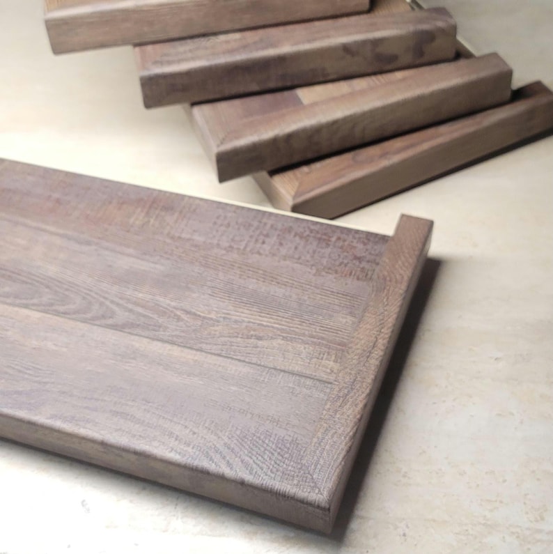May include: Close-up of several open end stair tread covers made of flooring planks with a natural wood grain finish. The treads are various custom sizes and shapes, with a warm brown color. The wood has an embossed in register appearance, suggesting a high end customization.
