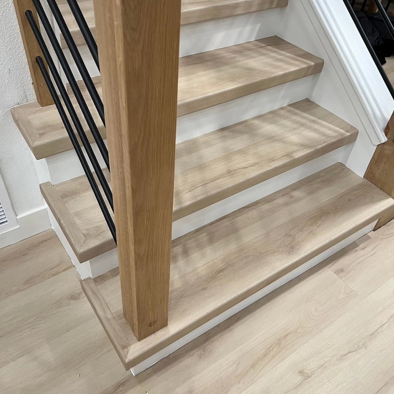 May include: A staircase with modern custom lvp steps and risers painted white. The stairs have a contemporary wooden newel post and black metal balusters. The flooring is light wood.