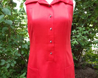 May include: A sleeveless, bright red vintage dress with a collared neckline and button-down front. The dress features two front pockets and is displayed on a mannequin. The dress is a classic style.