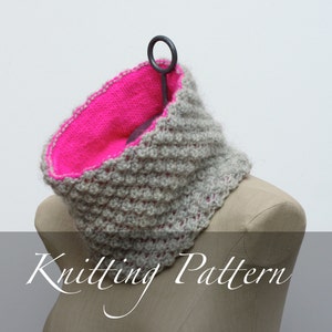 Könnte beinhalten: Ein grauer und rosa gestrickter Schal mit einem strukturierten Stichmuster. Der Schal wird auf einer Schaufensterpuppe präsentiert.