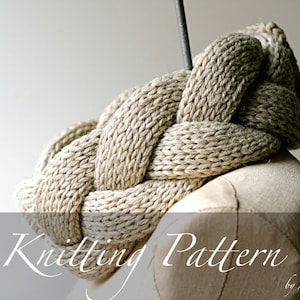 May include: A close-up of a knitted beige cowl neck scarf with a braided design. The scarf is displayed on a mannequin. The text "Knitting Pattern by Amy La Roux" is at the bottom of the image.