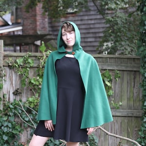 May include: A green hooded cape with brown buttons. The cape is made of a soft, warm fabric and has a simple, elegant design.