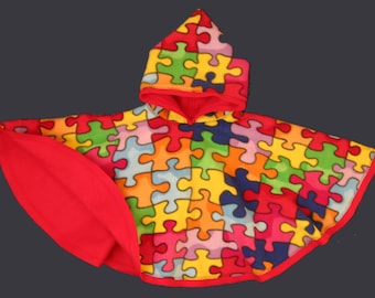 May include: A hooded poncho with a jigsaw puzzle design. The outer layer is patterned with multi-coloured puzzle pieces. The hood and interior are red. The poncho is designed to be worn as outerwear.
