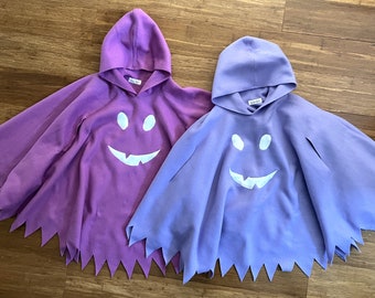 May include: Two purple and blue hooded ghost costumes with white smiling faces. The costumes have jagged edges around the bottom.