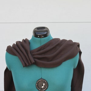 Puede incluir: Una bufanda marr&oacute;n drapeada sobre un maniqu&iacute; turquesa. La bufanda est&aacute; hecha de una tela suave y est&aacute; dise&ntilde;ada para crear un efecto de capas alrededor del cuello y los hombros. El fondo es una pared blanca lisa.