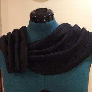 Puede incluir: Una bufanda negra drapeada sobre un maniqu&iacute; verde azulado. La bufanda est&aacute; hecha de una tela oscura y suave y est&aacute; dispuesta en pliegues fluidos. El maniqu&iacute; tiene una pieza de cuello negra.