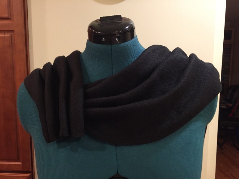 Puede incluir: Una bufanda negra drapeada sobre un maniqu&iacute; verde azulado. La bufanda est&aacute; hecha de una tela oscura y suave y est&aacute; dispuesta en pliegues fluidos. El maniqu&iacute; tiene una pieza de cuello negra.