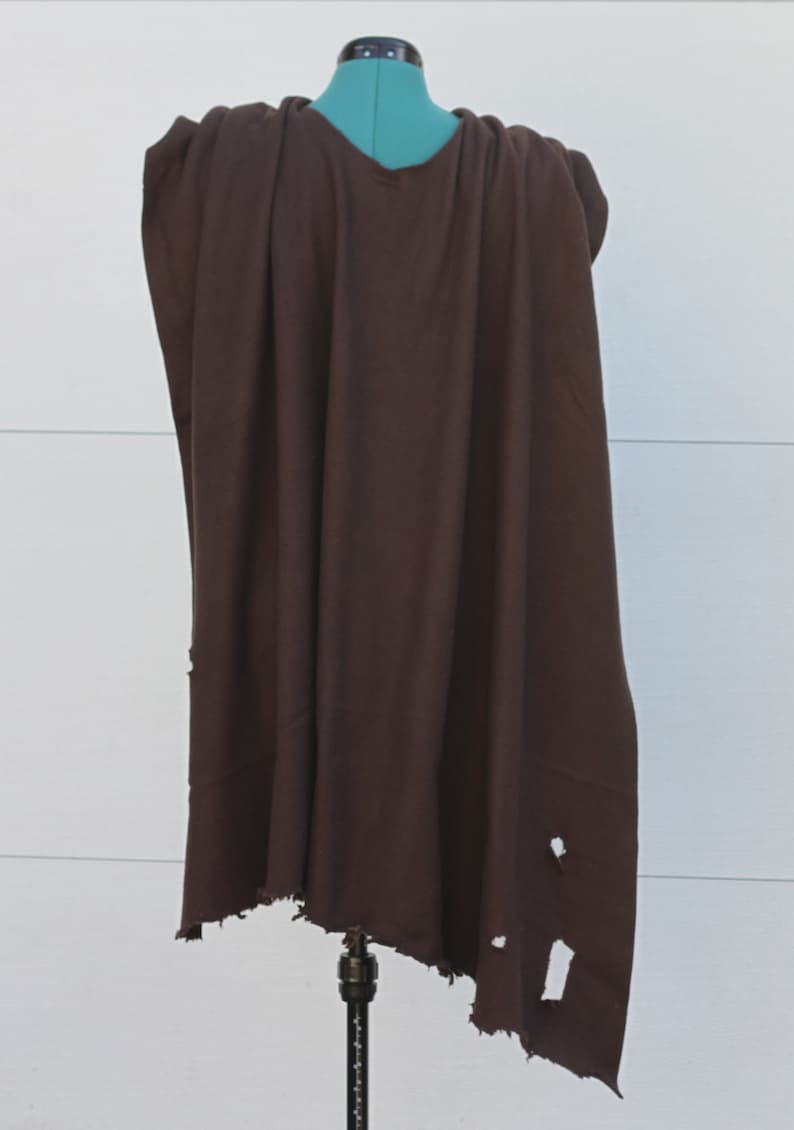 Puede incluir: Una capa marr&oacute;n oscuro con cuello en V, colocada sobre un maniqu&iacute;. La tela tiene un aspecto desgastado con varios agujeros cerca del borde inferior. La capa es probablemente para disfraces o cosplay.